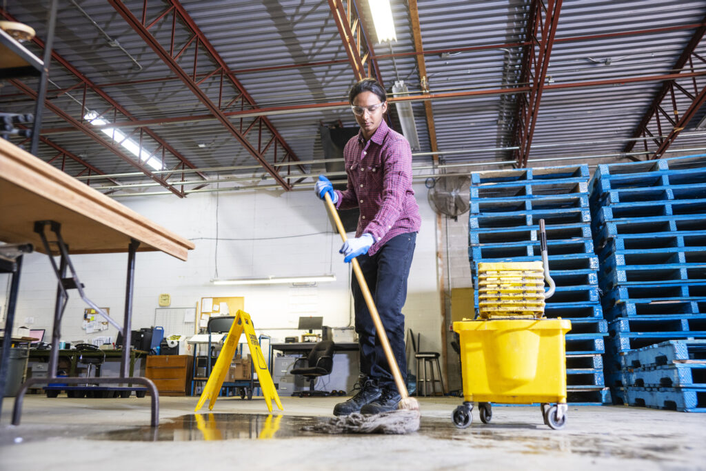 A worker in a warehouse cleaning-up a hazard of spilled liquid.