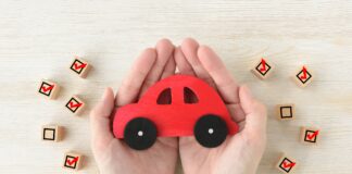 Car toy covered by human's hands surrounded by wooden blocks with checking marks